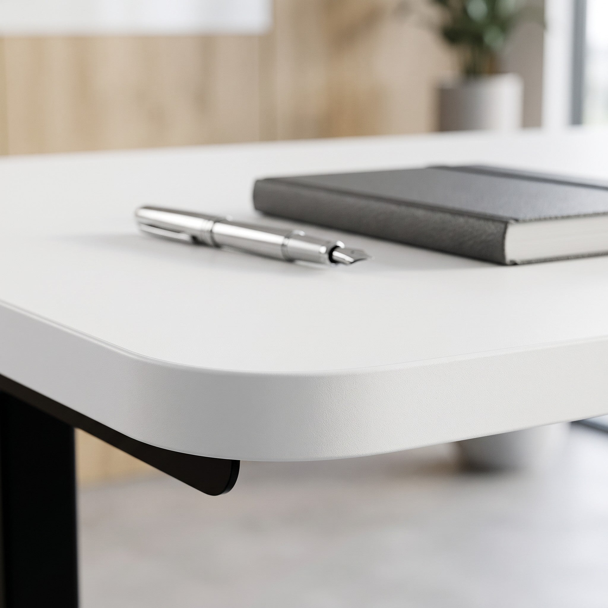 Close-up of a white Buro Syntra standing desk surface with rounded edges, a notebook, and a pen in a modern office.