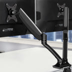 Black Studio dual gas-spring monitor arm holding two computer screens on a clean desk setup.