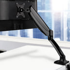 Black Studio gas-spring monitor arm clamped to a white desk, holding a computer display in a modern office.