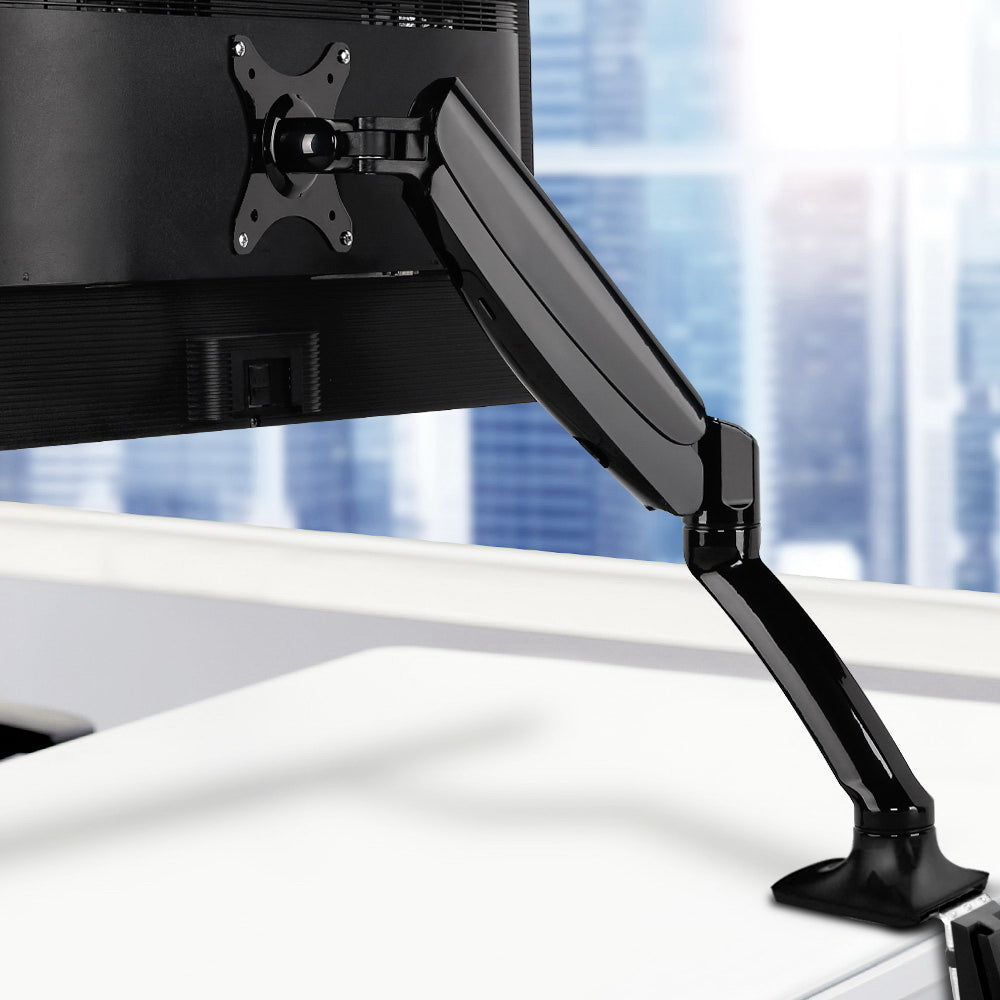 Black Studio gas-spring monitor arm clamped to a white desk, holding a computer display in a modern office.
