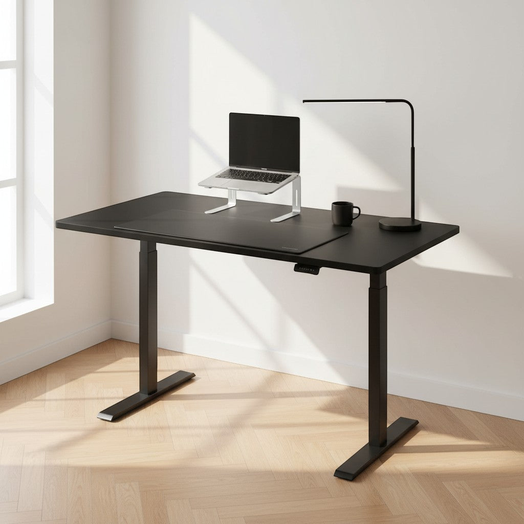 Cloud Office Studio 140cm black dual-motor standing desk with matte finish, laptop stand, and lamp in a bright office.
